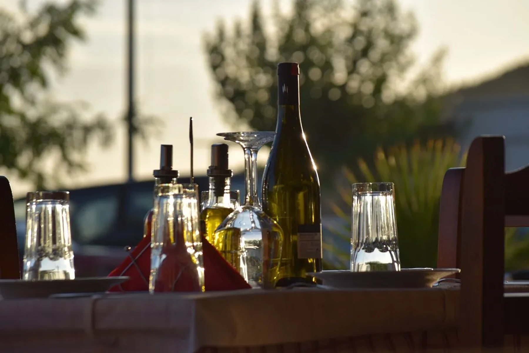 A laid table at Restaurant Kolagji late in the day — a bottle of wine, two cruets, upturned glasses and a folded red napkin