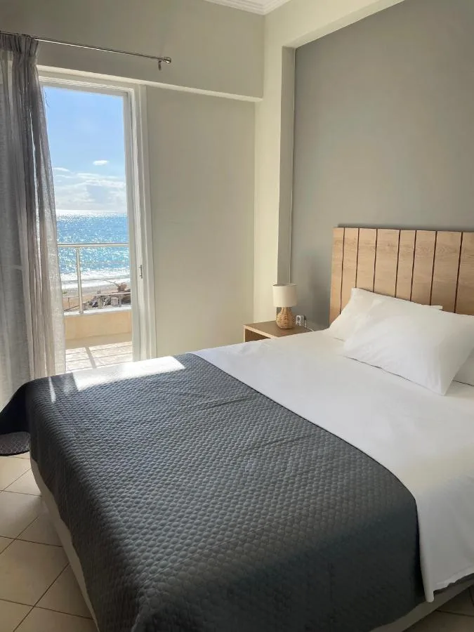 A double bed with a grey quilted throw beside an open balcony door with sunlight on the sea outside