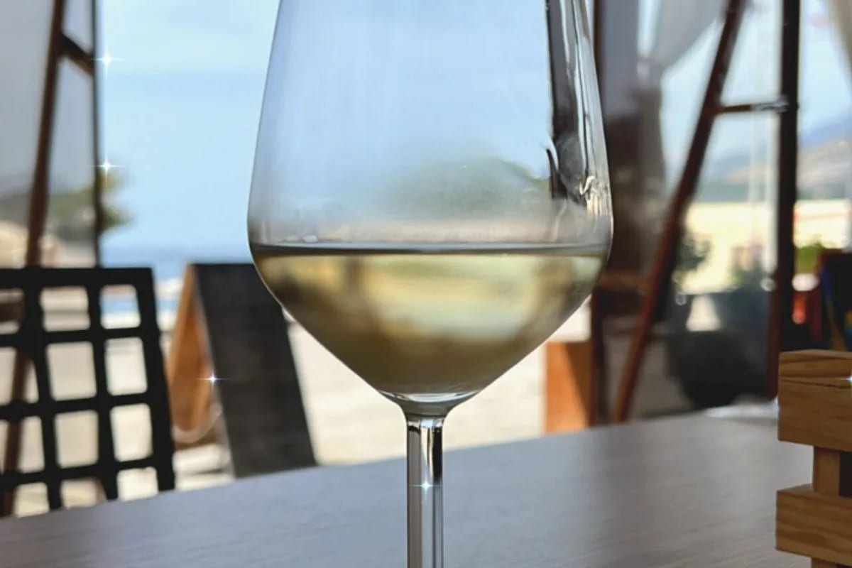 A glass of white wine on a table in daylight, the beach and the sea out of focus behind it