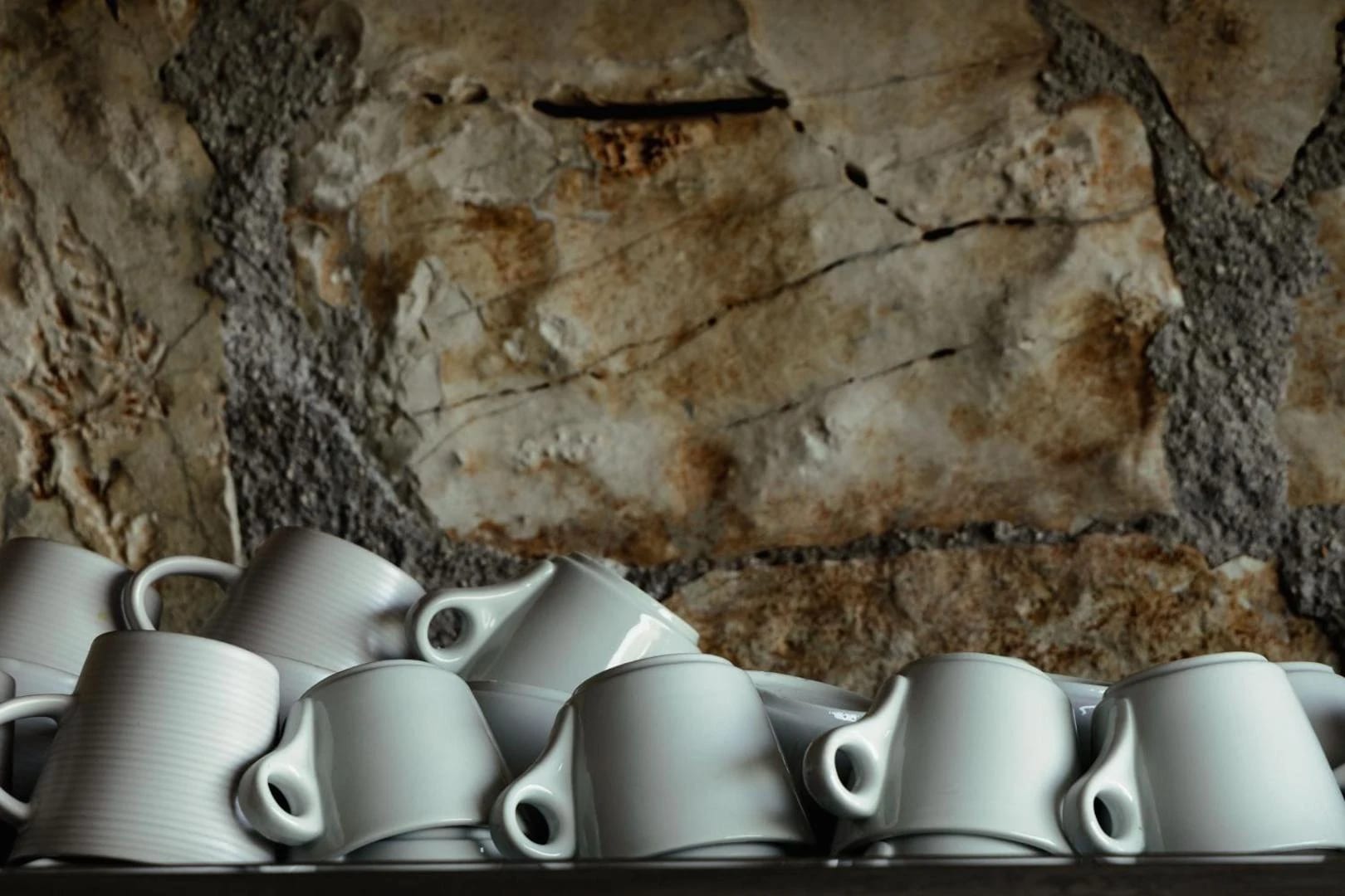 Stacked white coffee cups on a shelf against the stone wall