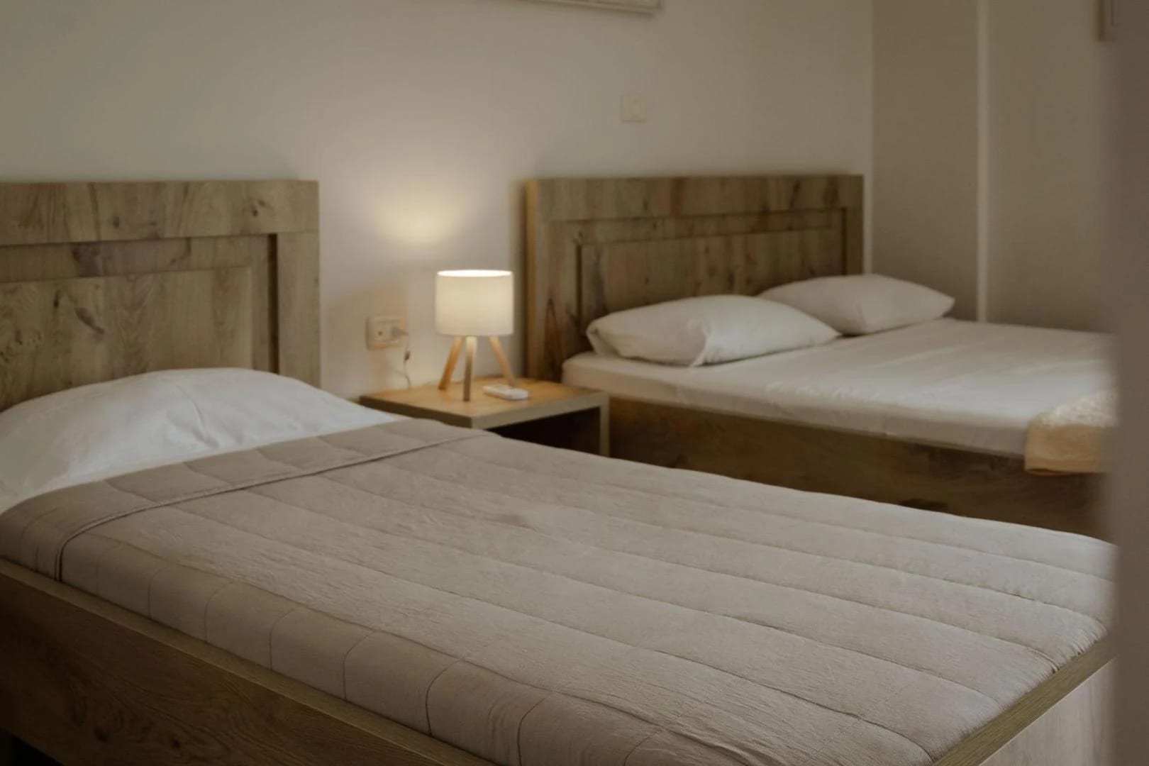 A queen bed and a single bed side by side with timber headboards and a lamp between them