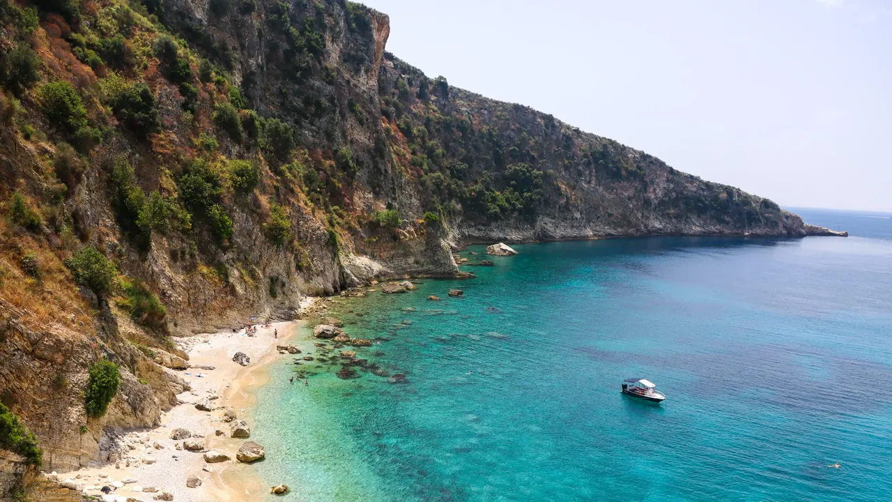 The cliff-enclosed cove of Filikuri seen from above, turquoise water against pale rock