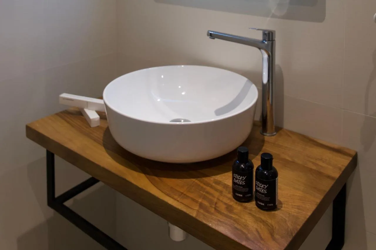 A round white vessel basin on a live-edge oak shelf with a black steel frame and two Lush bottles