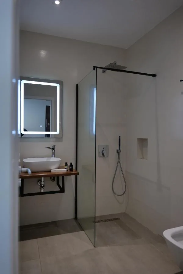 A bathroom with a walk-in rain shower behind glass and a backlit square mirror over a vessel basin