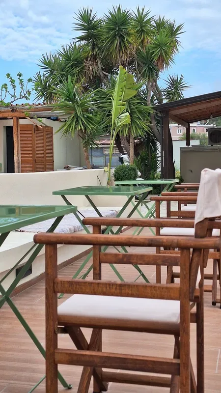 Green folding bistro tables and wooden armchairs on a planted terrace under dracaena palms