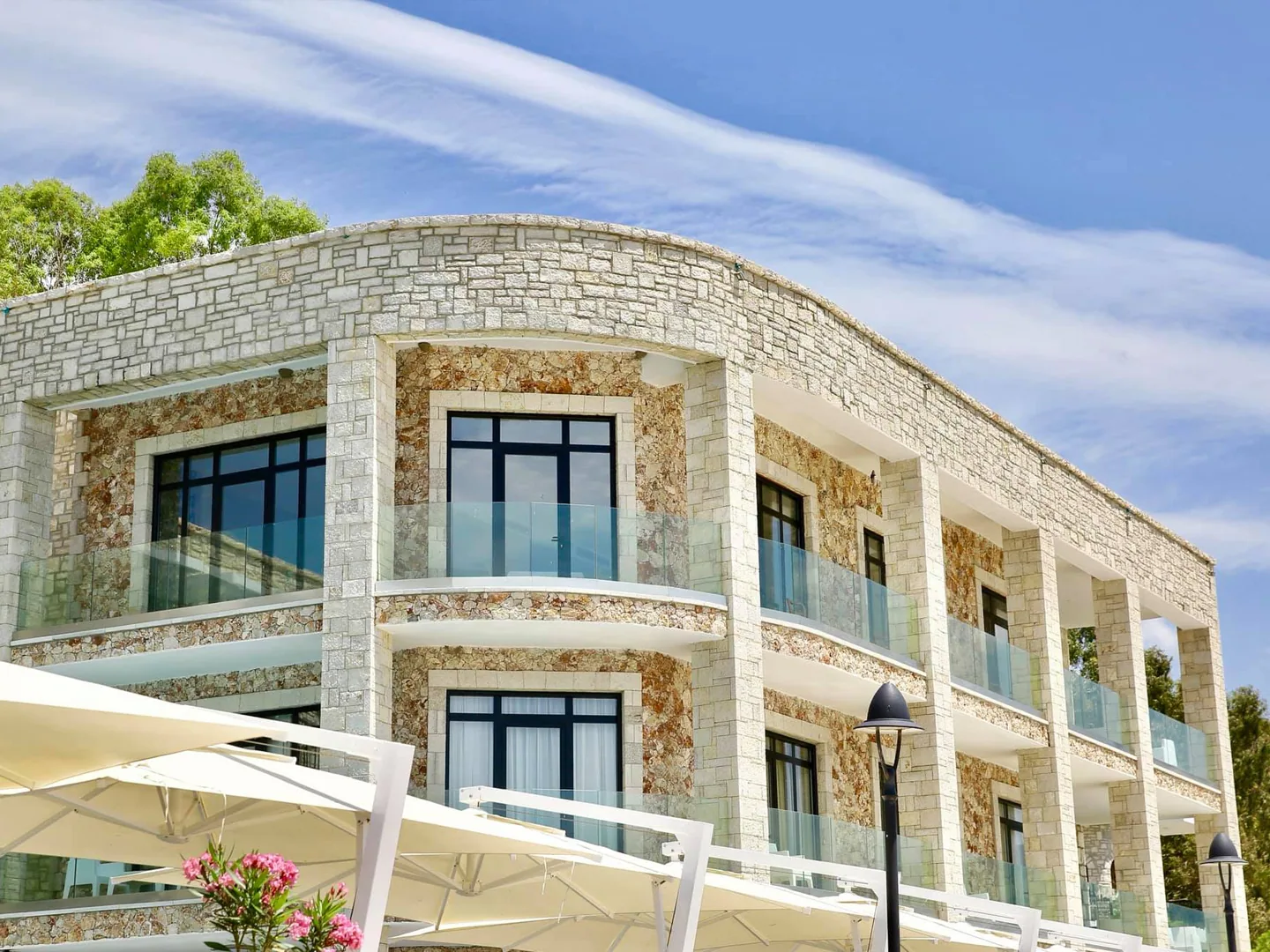 A close view of the hotel's coursed limestone facade, its arched windows and iron balconies, with white parasols on the terrace below