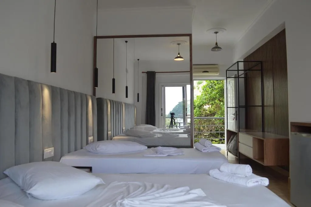 Beds made up in white along a full-width padded headboard, with a balcony beyond