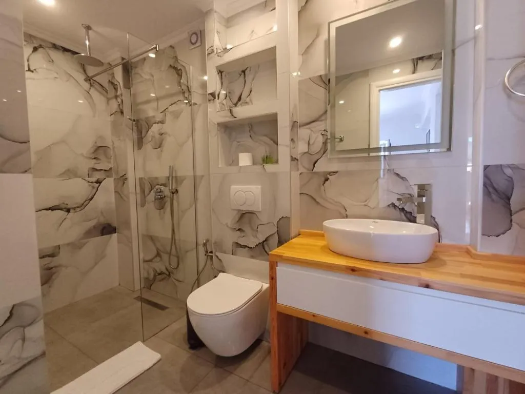 A bathroom at Velco BB Himara with a walk-in shower, marble-pattern tile and a timber vanity