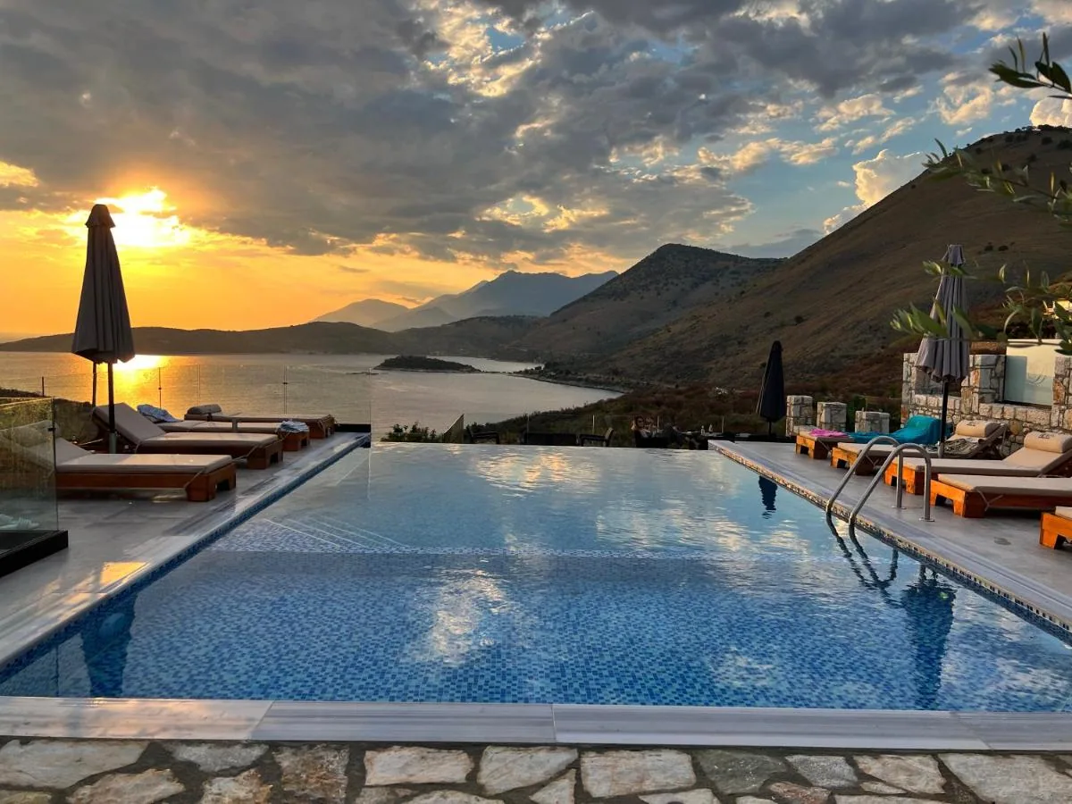 The infinity pool at sunset, loungers along both sides, the sun going down over the bay of Porto Palermo