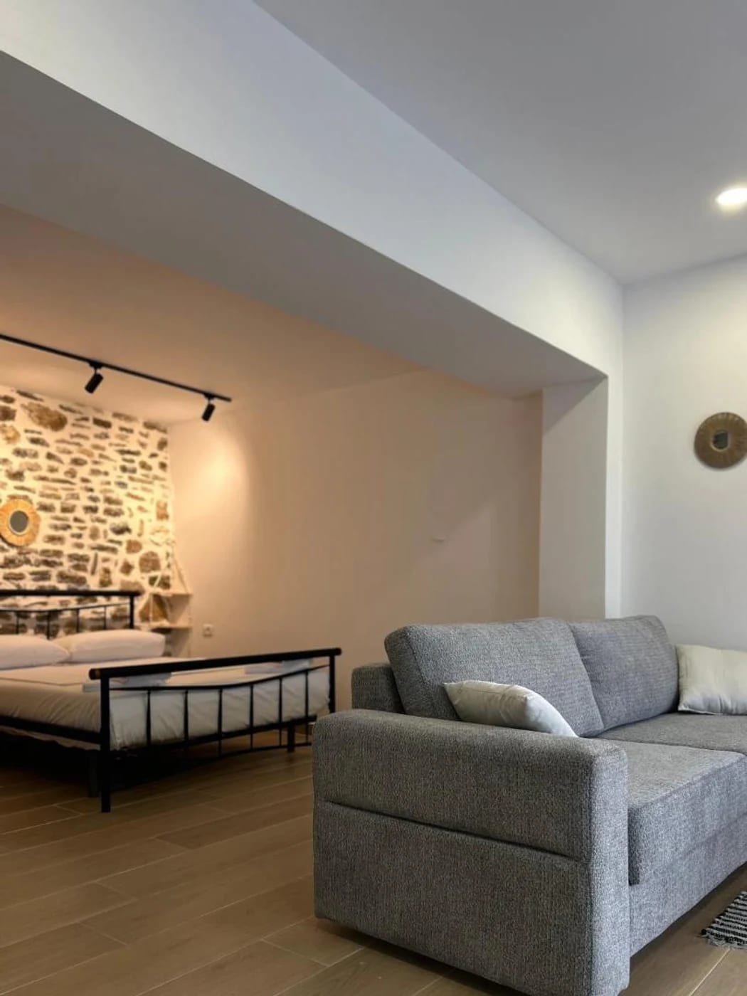Open-plan studio with a grey sofa, an iron bed and a stone accent wall behind