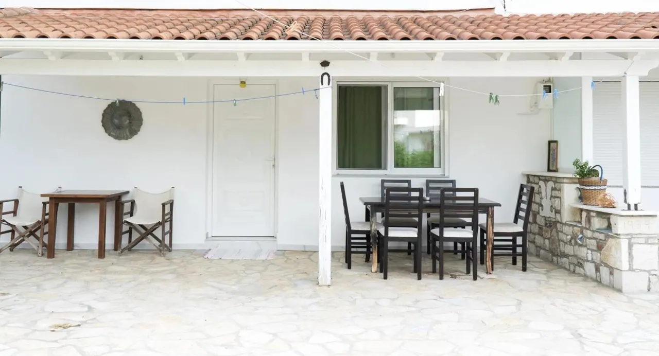 The covered terrace of the stone house, with a long table under a tiled roof