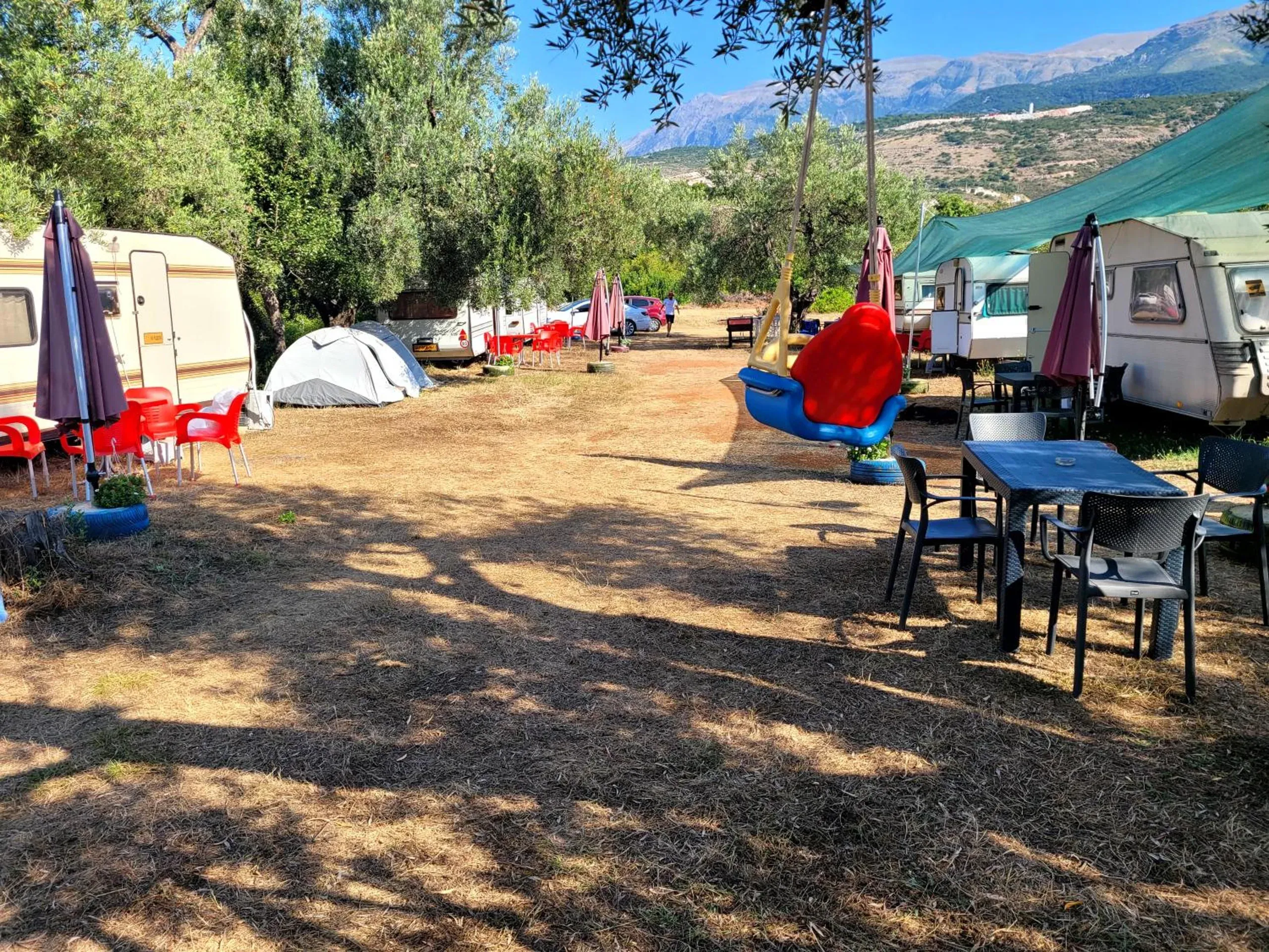 Caravans with wine-coloured parasols and red chairs along the lane through the olive grove at Aquariumi Jale Camping