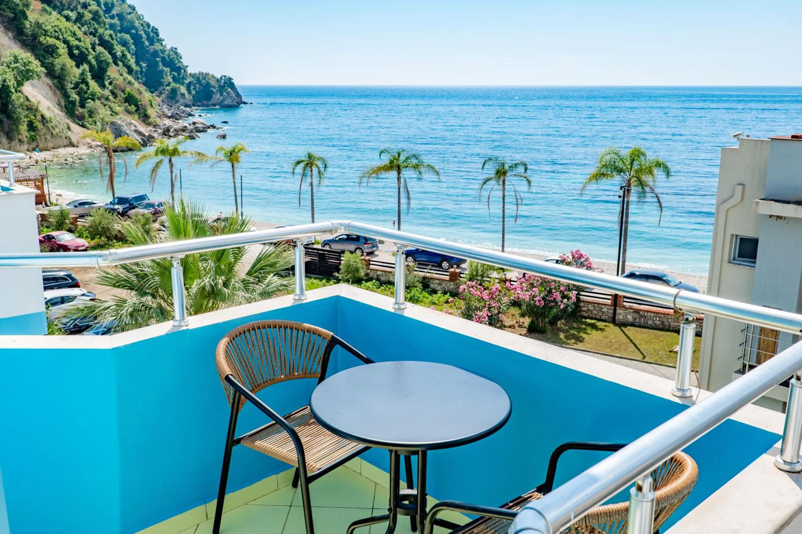 A cerulean balcony at Blue Stay Boutique Hotel in Himara, a table and chairs looking over the palms to Potam Beach and the sea