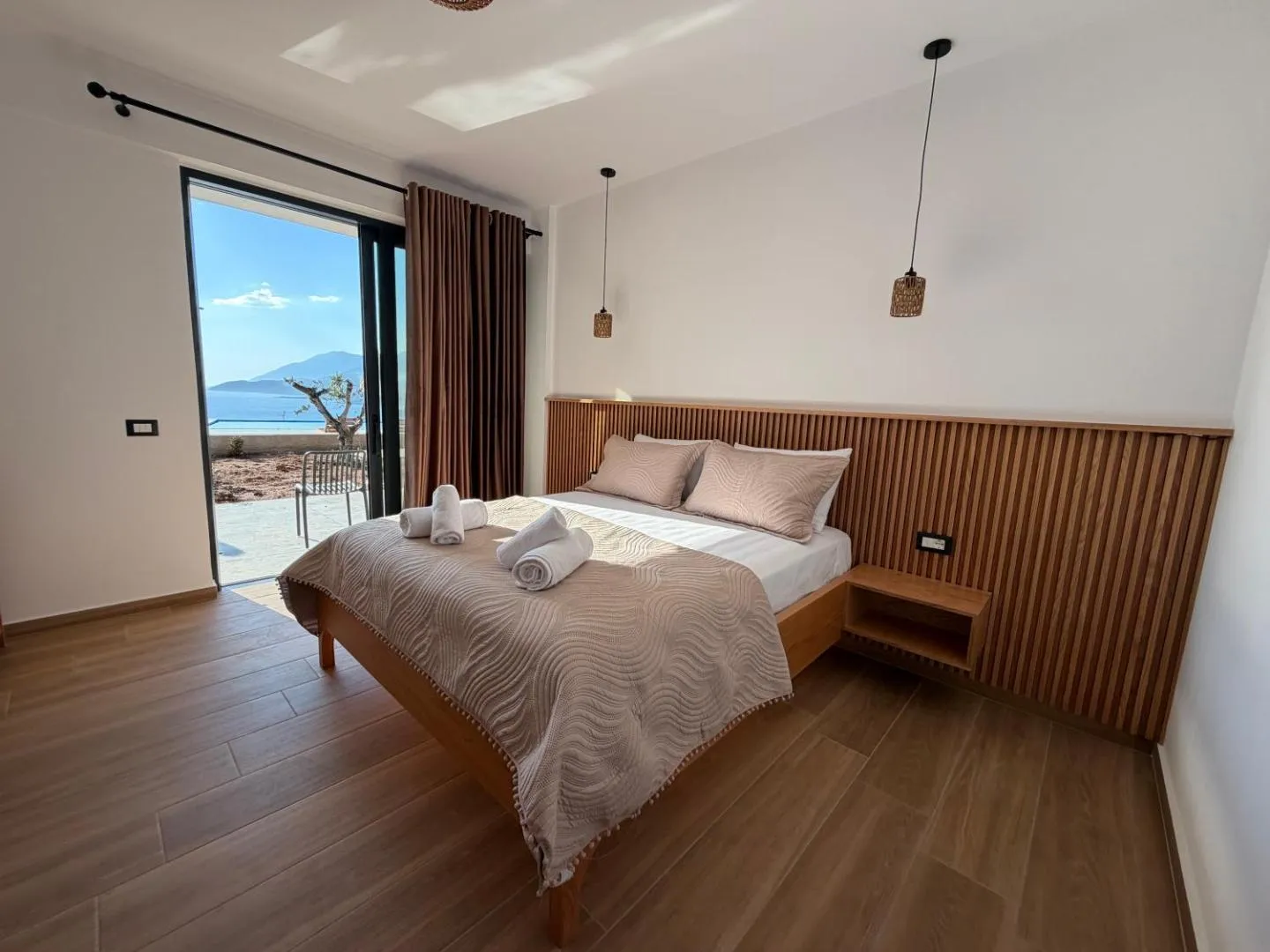 A double bed with an oak slat headboard beside an open balcony door looking over the sea at Filikuri Boutique Hotel
