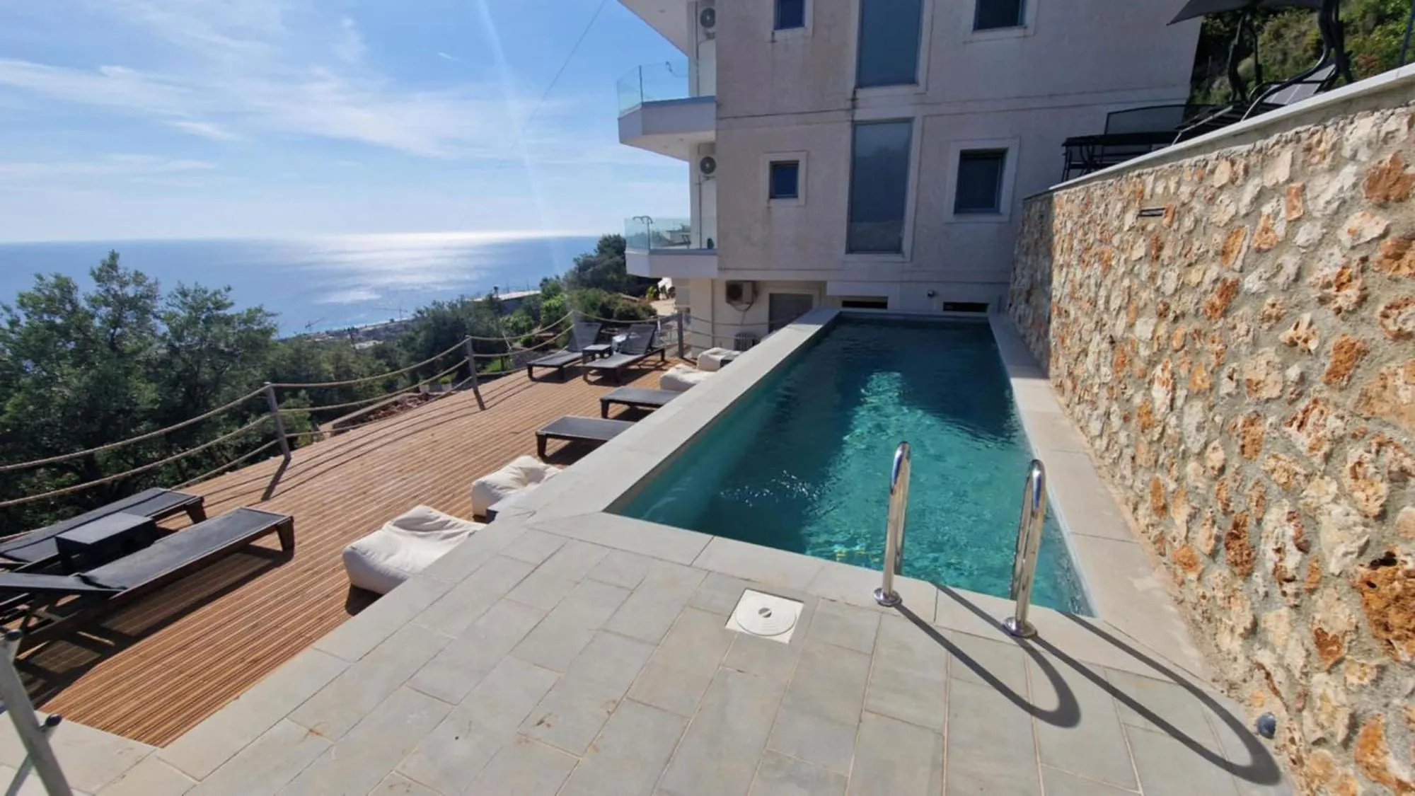 The pool at Ionian Pearl between a drystone wall and a timber deck, with the sea beyond, above Drymades, Dhërmi