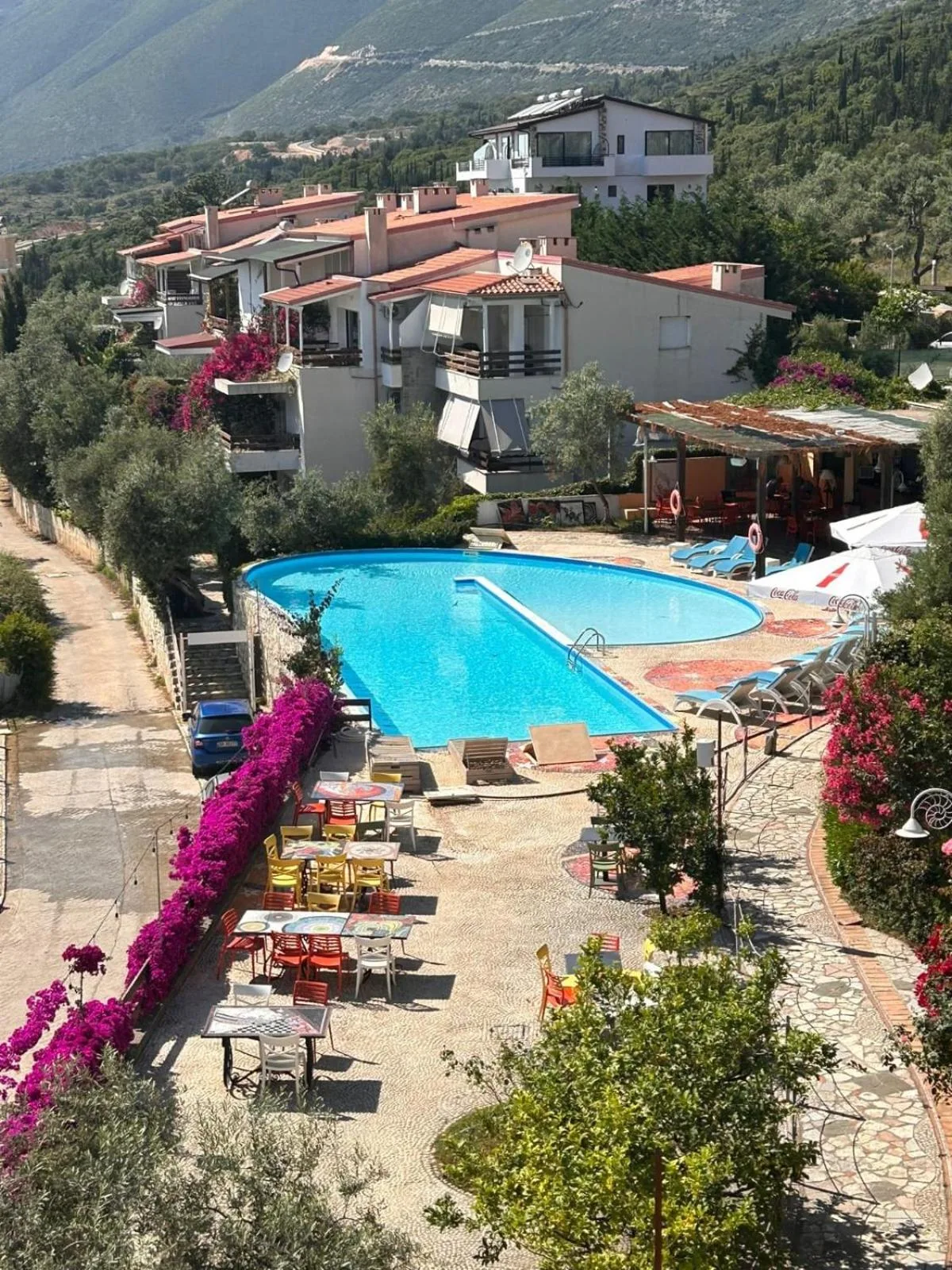 The pool at Olives Residence seen from above, with white villas, olive trees and bougainvillea in Drymades, Dhërmi