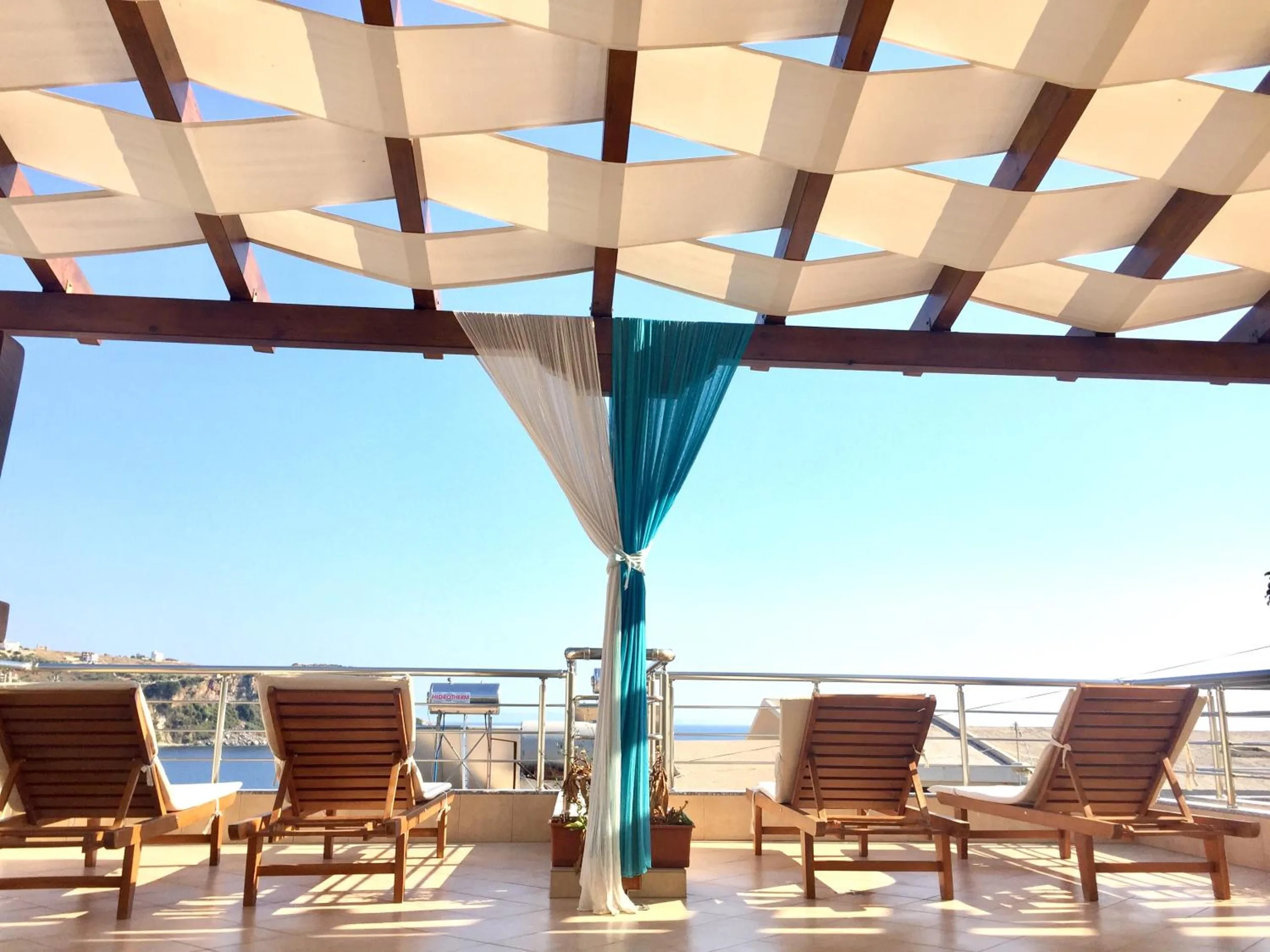 The roof terrace of Vila Kosteli in Himara, with wooden loungers under a woven canvas pergola and the sea beyond